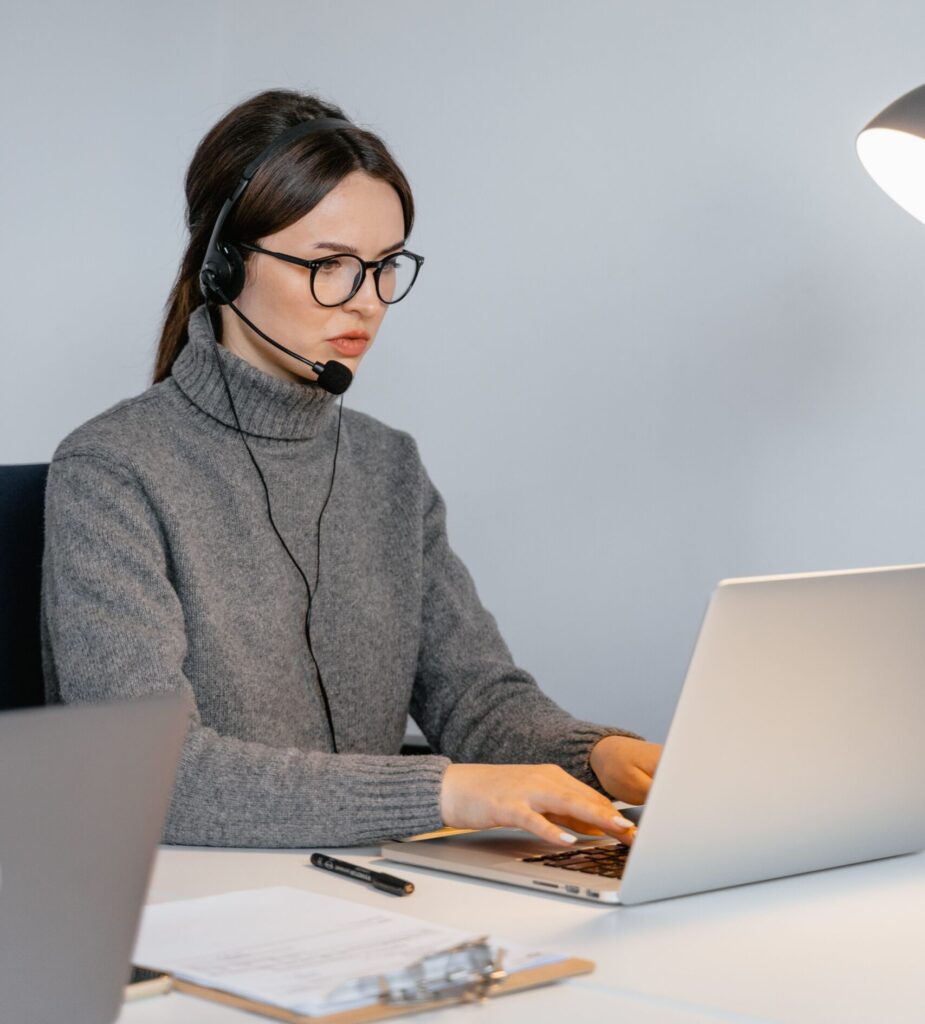 Focused woman in office with headset, providing customer support on laptop.